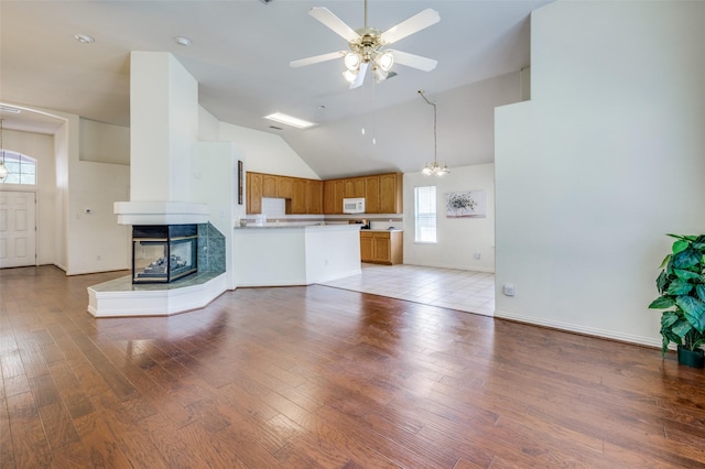 unfurnished living room with high vaulted ceiling, light wood-style flooring, ceiling fan with notable chandelier, a multi sided fireplace, and baseboards