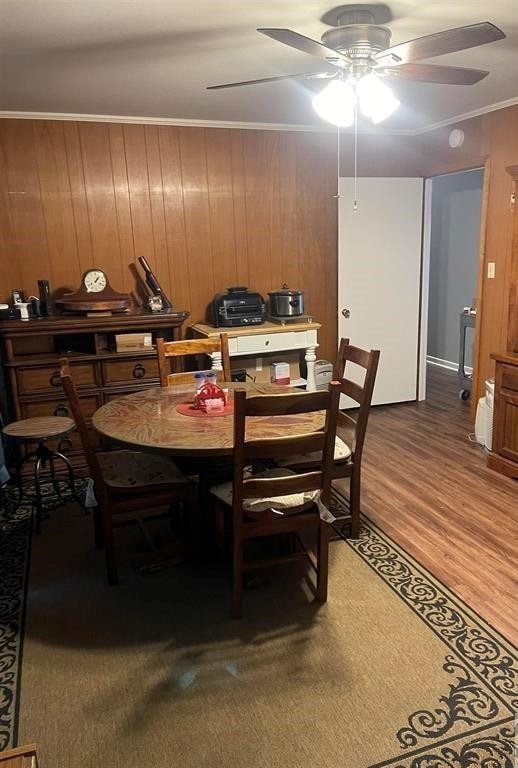 dining space with crown molding, hardwood / wood-style floors, wood walls, and ceiling fan