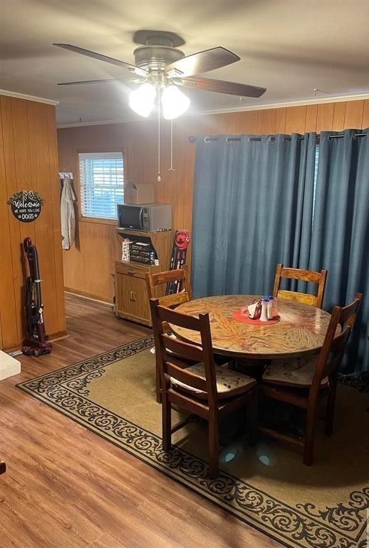 dining area featuring ornamental molding, hardwood / wood-style floors, ceiling fan, and wooden walls