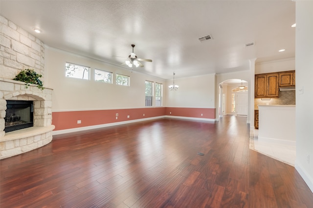 unfurnished living room featuring ceiling fan with notable chandelier, hardwood / wood-style flooring, ornamental molding, and a stone fireplace