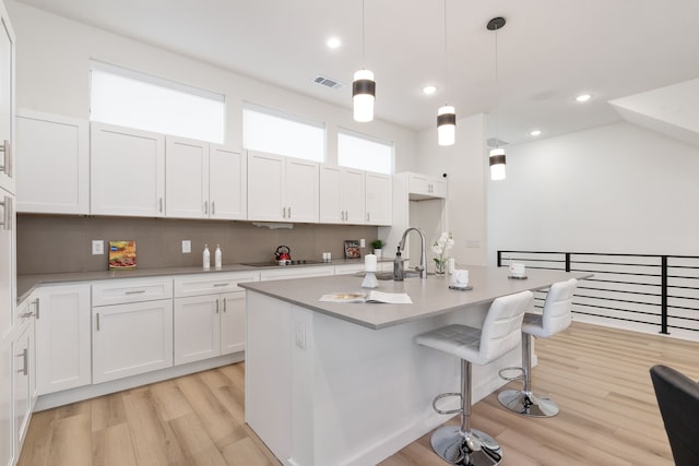 kitchen featuring a kitchen breakfast bar, pendant lighting, light hardwood / wood-style flooring, white cabinetry, and an island with sink