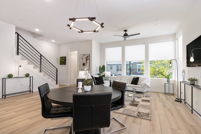 dining area with ceiling fan with notable chandelier and light hardwood / wood-style flooring