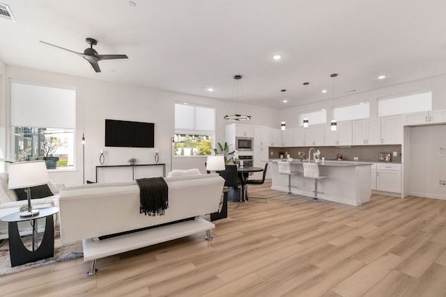 living room featuring ceiling fan, light wood-type flooring, and sink