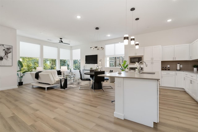 kitchen with pendant lighting, a kitchen island with sink, white cabinets, sink, and ceiling fan