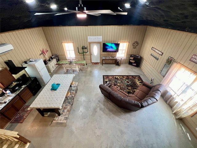 unfurnished living room with concrete flooring, ceiling fan, and wood walls