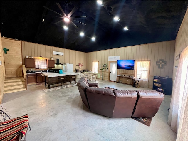 living area with an AC wall unit, wood walls, vaulted ceiling, and concrete floors