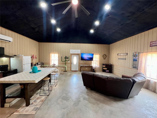 living area with vaulted ceiling, a ceiling fan, finished concrete floors, and wood walls