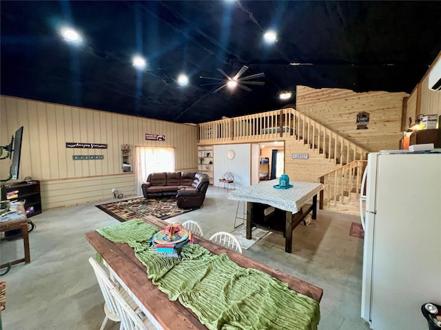 dining space featuring unfinished concrete floors, wood walls, and a ceiling fan