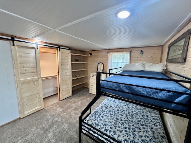 unfurnished bedroom with a barn door, wood walls, and carpet flooring