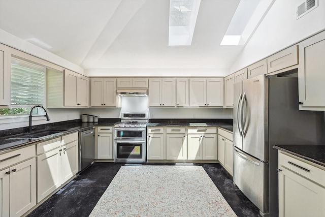 kitchen with stainless steel appliances, sink, dark stone countertops, and vaulted ceiling with skylight