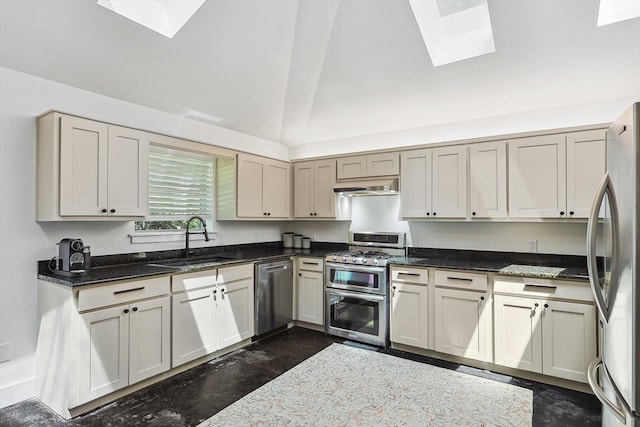 kitchen with vaulted ceiling with skylight, sink, appliances with stainless steel finishes, and dark stone counters