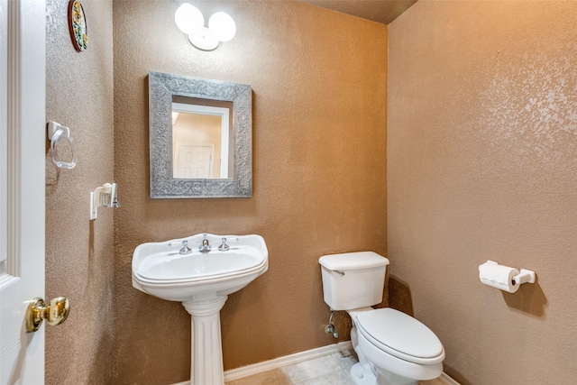 bathroom with toilet, baseboards, and a textured wall