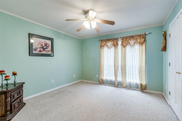 carpeted empty room featuring crown molding, a ceiling fan, and baseboards