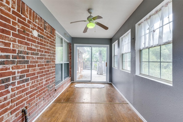 doorway to outside featuring brick wall, a textured wall, baseboards, and wood-type flooring