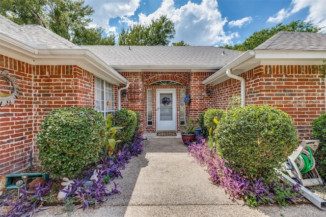 view of exterior entry with brick siding and a shingled roof