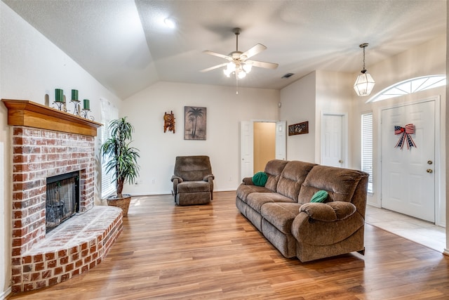 living room with light wood-type flooring, a fireplace, a textured ceiling, ceiling fan, and vaulted ceiling