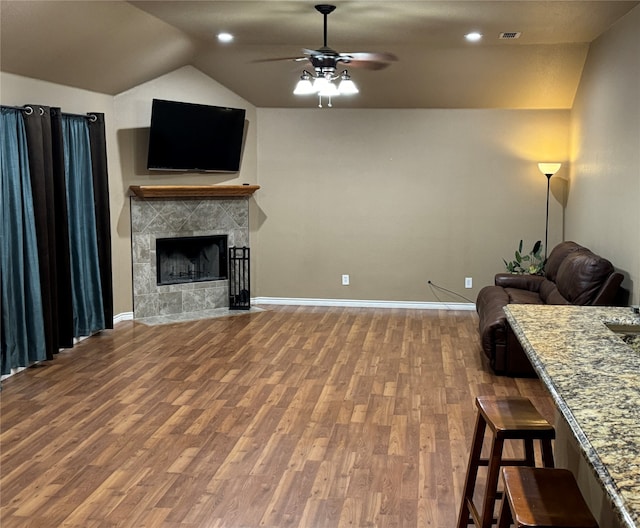 living room with lofted ceiling, ceiling fan, a tile fireplace, and hardwood / wood-style flooring