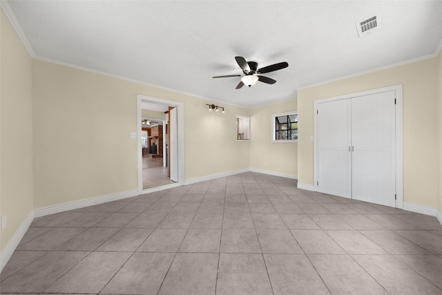 empty room with ceiling fan, light tile patterned floors, visible vents, baseboards, and crown molding