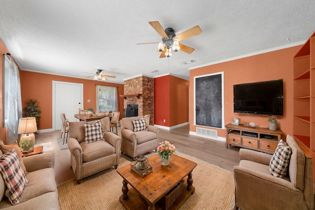 living room with visible vents, crown molding, a textured ceiling, light wood-style floors, and a fireplace