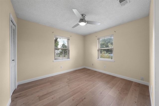 unfurnished room with ceiling fan, a textured ceiling, visible vents, baseboards, and light wood-style floors