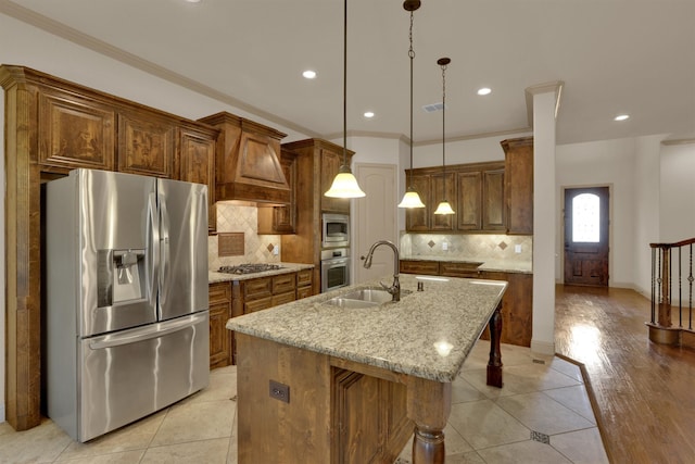 kitchen featuring custom exhaust hood, stainless steel appliances, light stone countertops, a center island with sink, and light hardwood / wood-style floors