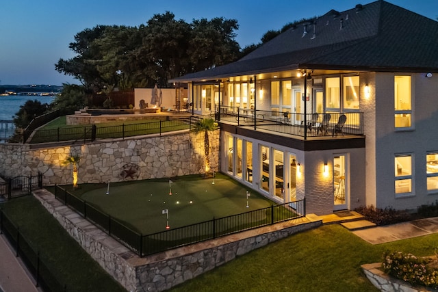 back house at dusk with a balcony, a yard, and a patio