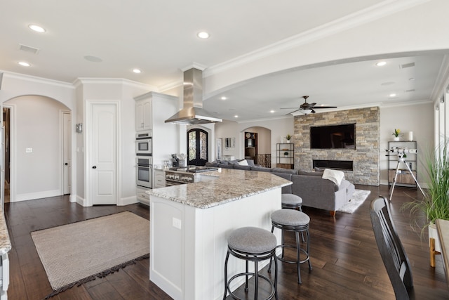 kitchen featuring ornamental molding, island range hood, white cabinetry, a kitchen bar, and dark hardwood / wood-style flooring