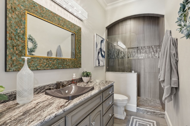 bathroom with ornamental molding, vanity, toilet, and tiled shower