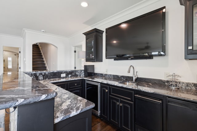 kitchen with beverage cooler, dark stone counters, crown molding, and sink