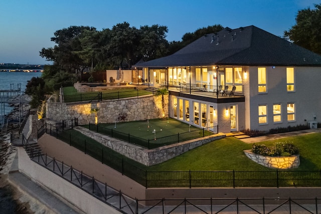 back house at dusk featuring a yard, a water view, and a balcony