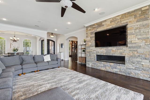 living room with ceiling fan with notable chandelier, a fireplace, crown molding, and dark hardwood / wood-style flooring