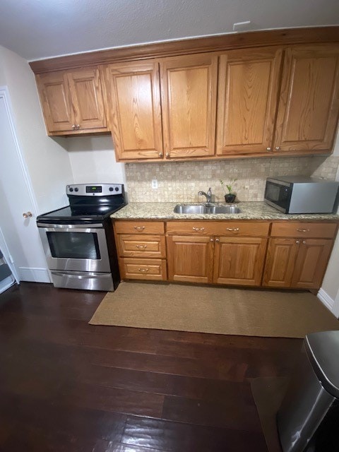 kitchen with appliances with stainless steel finishes, light stone countertops, sink, dark hardwood / wood-style floors, and tasteful backsplash