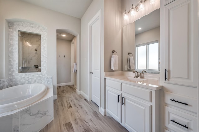 full bath featuring a garden tub, vanity, wood finished floors, baseboards, and a walk in shower