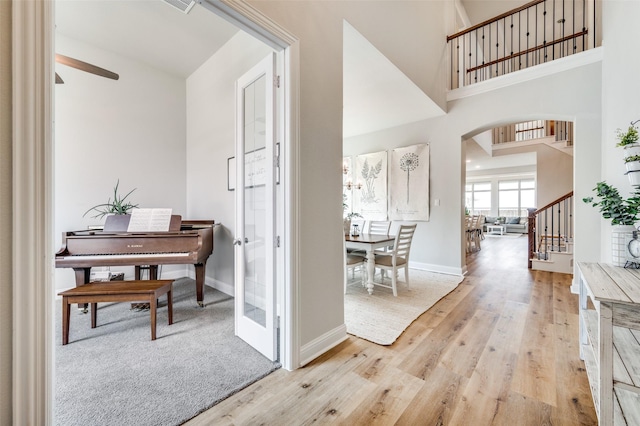 hallway featuring arched walkways, light wood finished floors, stairway, a high ceiling, and baseboards