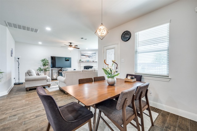 dining area with ceiling fan, a fireplace, visible vents, and wood finished floors