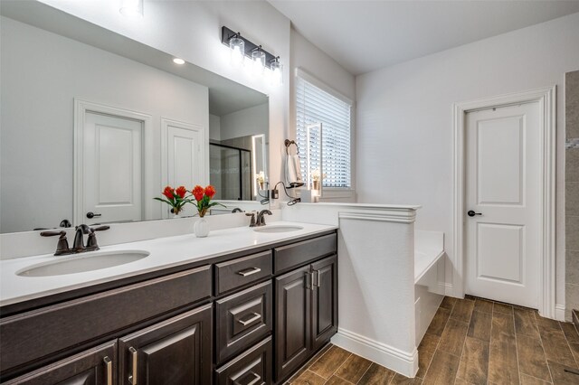 bathroom featuring wood finish floors, a sink, a shower stall, a bath, and double vanity