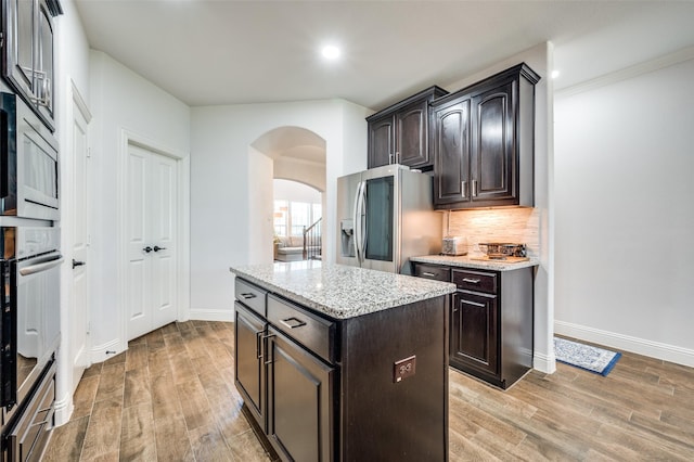 kitchen with arched walkways, appliances with stainless steel finishes, light wood-type flooring, and backsplash