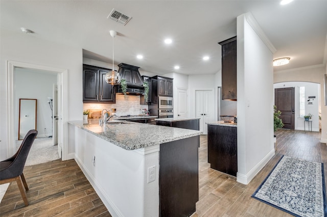 kitchen with arched walkways, appliances with stainless steel finishes, a sink, wood tiled floor, and backsplash