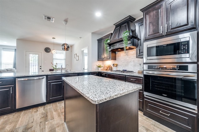 kitchen featuring custom exhaust hood, stainless steel appliances, visible vents, decorative backsplash, and light wood-style floors