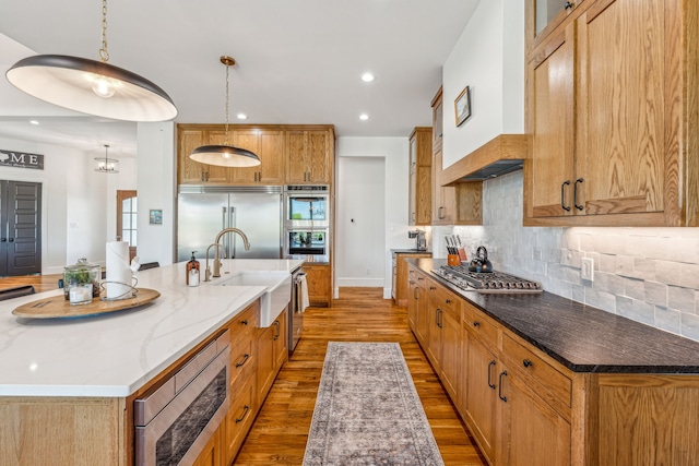 kitchen with a large island, sink, built in appliances, pendant lighting, and hardwood / wood-style flooring