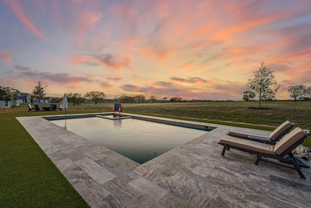 pool at dusk featuring a lawn and a patio area