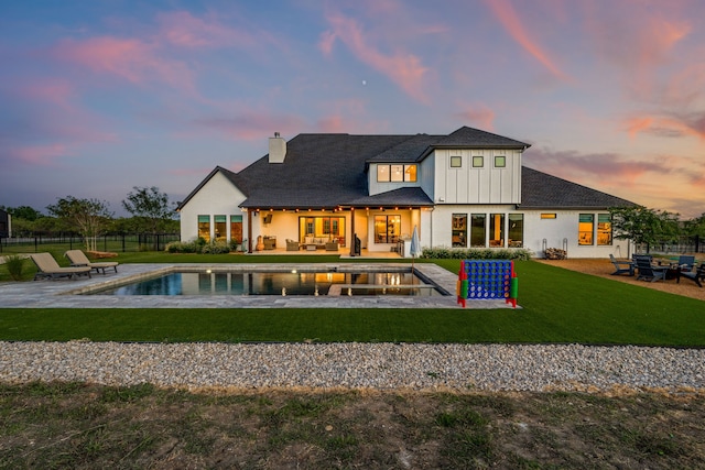 back house at dusk with a fenced in pool, a patio area, a yard, and an outdoor hangout area