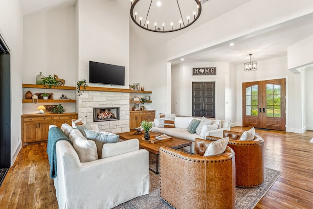 living room with a chandelier, a high ceiling, light wood-type flooring, and a stone fireplace