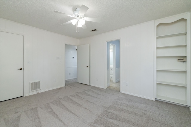 unfurnished bedroom featuring a textured ceiling, light colored carpet, ceiling fan, and ensuite bath