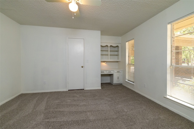 unfurnished bedroom featuring a textured ceiling, built in desk, carpet, and ceiling fan