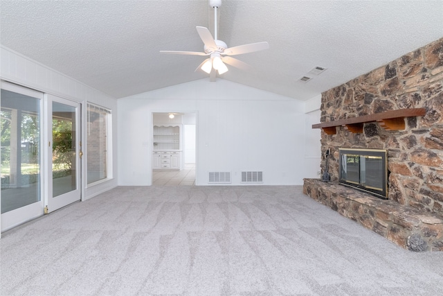 unfurnished living room with a textured ceiling, vaulted ceiling, a fireplace, light colored carpet, and ceiling fan