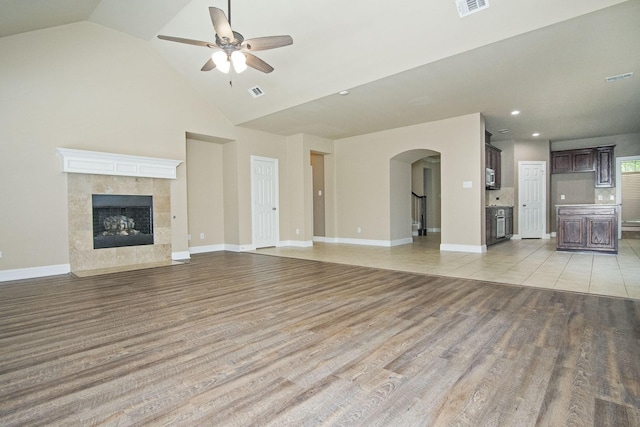 unfurnished living room featuring light wood-type flooring, ceiling fan, a premium fireplace, and high vaulted ceiling