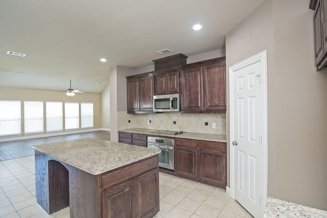 kitchen featuring ceiling fan, appliances with stainless steel finishes, light tile patterned floors, a kitchen island, and decorative backsplash