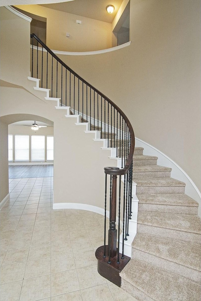 stairs featuring a towering ceiling, ceiling fan, and tile patterned floors