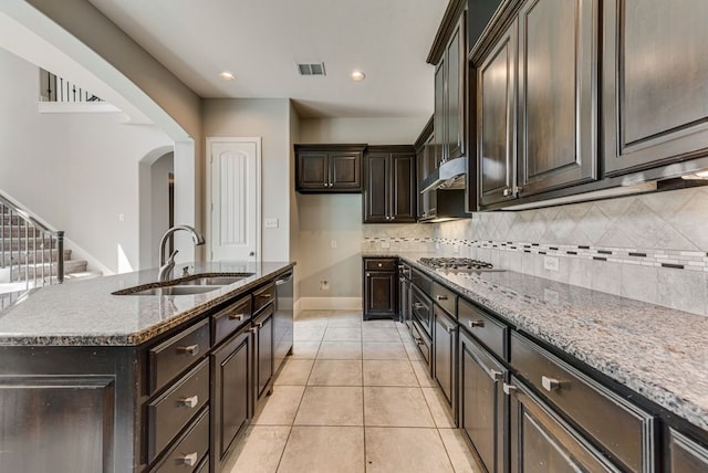 kitchen featuring a kitchen island with sink, light stone counters, sink, decorative backsplash, and appliances with stainless steel finishes